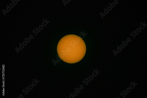 Tarcza słoneczna sfotografowana z użyciem teleobiektywu. W wyniku zastosowania filtra optycznego uzyskano ciepłą barwę tarczy słonecznej. Widoczne są plamy na powierzchni słońca.