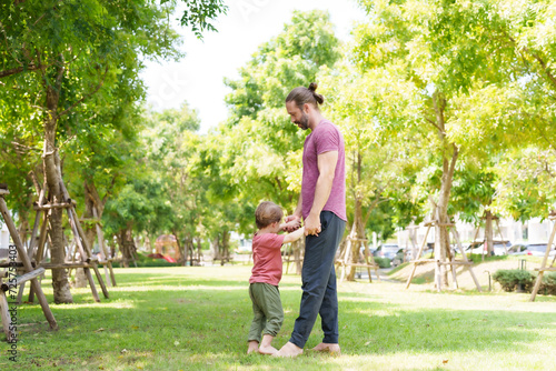 Caucasian father mother hold their little son hand, holding each child's hand lifting up, father mother take their adorable son for walk in picnic park on nice, sunny day, three feet touched grass.