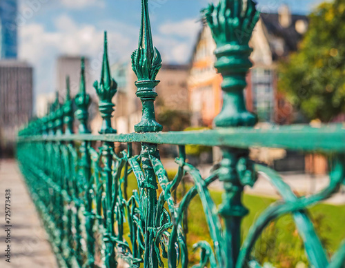 Green metal mesh fence that using to barricade the area, scene with blurred background of city outdoor place. Close-up and selective focus.