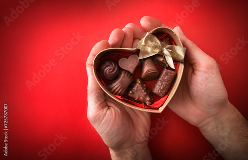 Red background with heart box of chocolates between the hands