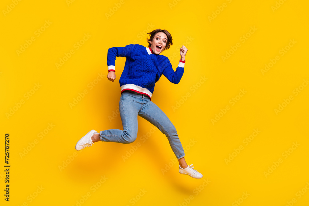 Full length photo of funny lucky lady dressed knitted sweater rising fists jumping high empty space isolated yellow color background