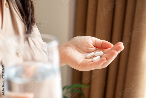Woman hand holding pill and glass of water, emergency medicine documents, supplements or antibiotic antidepressant painkillers to relieve pain, side effect symptoms, close view photo