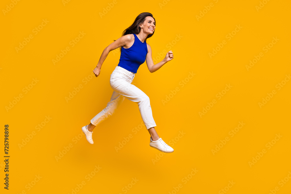 Full length photo of excited shiny woman wear blue top jumping running fast empty space isolated yellow color background