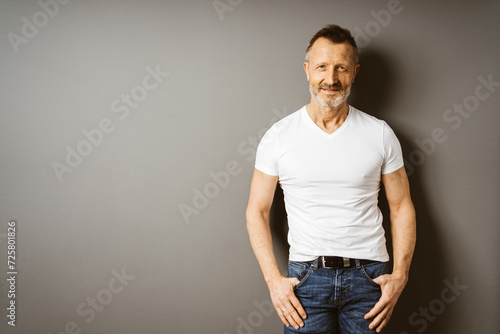 Active Older Man in White T-Shirt Standing Against Brown Wall, Smiling at the Camera with Copy Space
