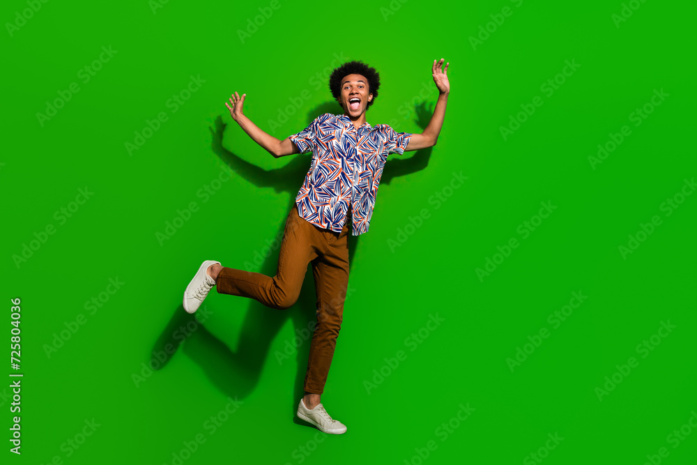 Full length photo of good mood positive guy wear print shirt dancing having fun isolated green color background Full length photo of good mood positive guy wear print shirt dancing having fun isolated green color background