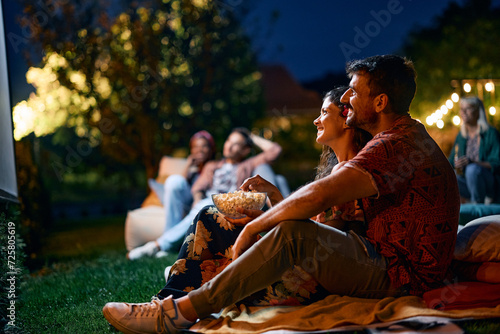 Fotografie Happy couple relaxing during movie night with friends in backyard