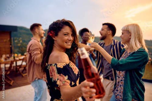 Happy woman toasting while having party with friends at sunset and looking at camera. © Drazen