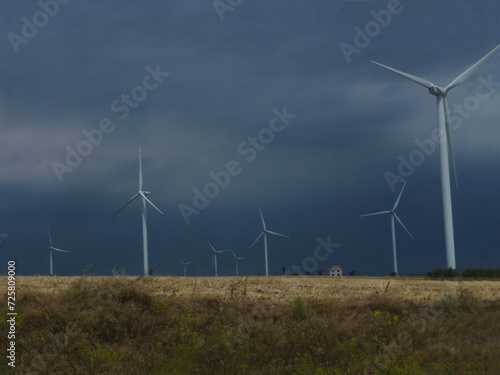 Wind generators are built on a wheat field against the background of a stormy sky.