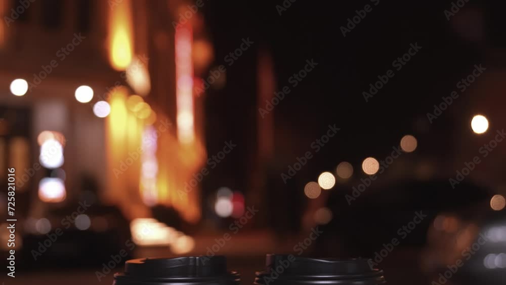 Two white paper disposable cups with black lids on blurred background of evening city lights. Hot Takeaway Coffee Outdoors. Street food, urban lifestyle concept. Copy space, space for text. Two white paper disposable cups with black lids on blurred background of evening city lights. Hot Takeaway Coffee Outdoors. Street food, urban lifestyle concept. Copy space, space for text.