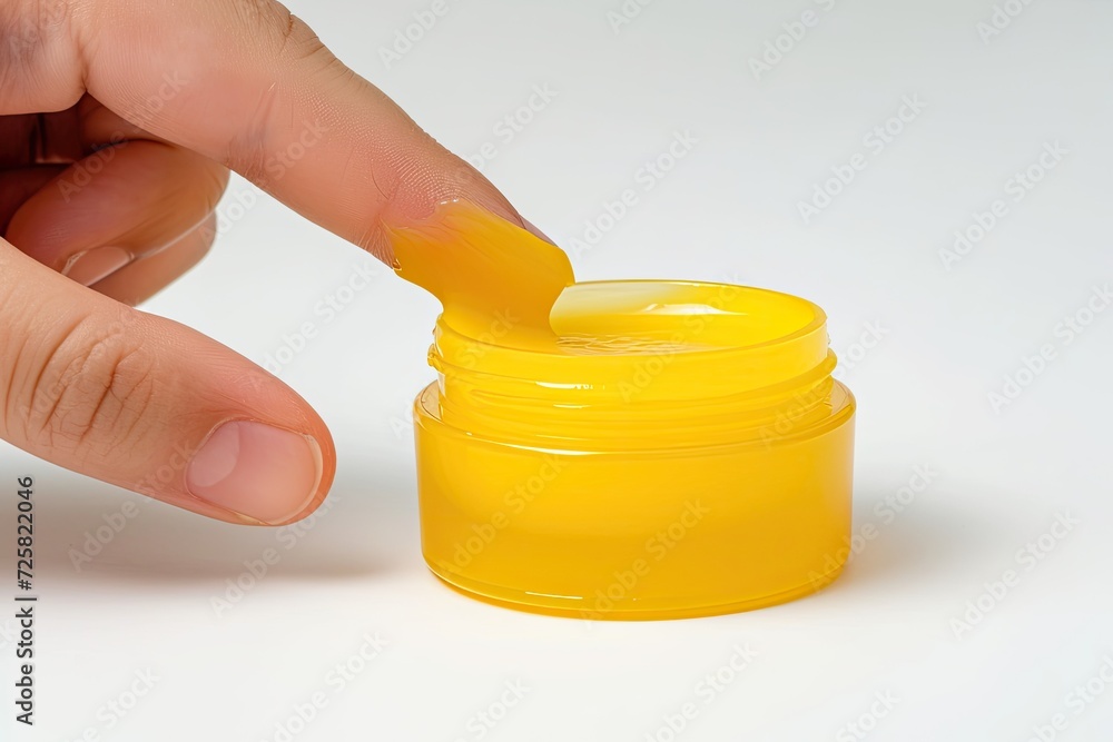 The image shows a finger and a yellow jar of vaseline balm on a white background The vaseline can be used as lip balm or for lubrication purposes The image shows a finger and a yellow jar of vaseline balm on a white background The vaseline can be used as lip balm or for lubrication purposes