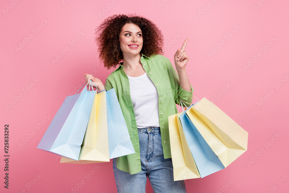 Photo portrait of pretty young girl hold shopping bags point empty space wear trendy green outfit isolated on pink color background Photo portrait of pretty young girl hold shopping bags point empty space wear trendy green outfit isolated on pink color background