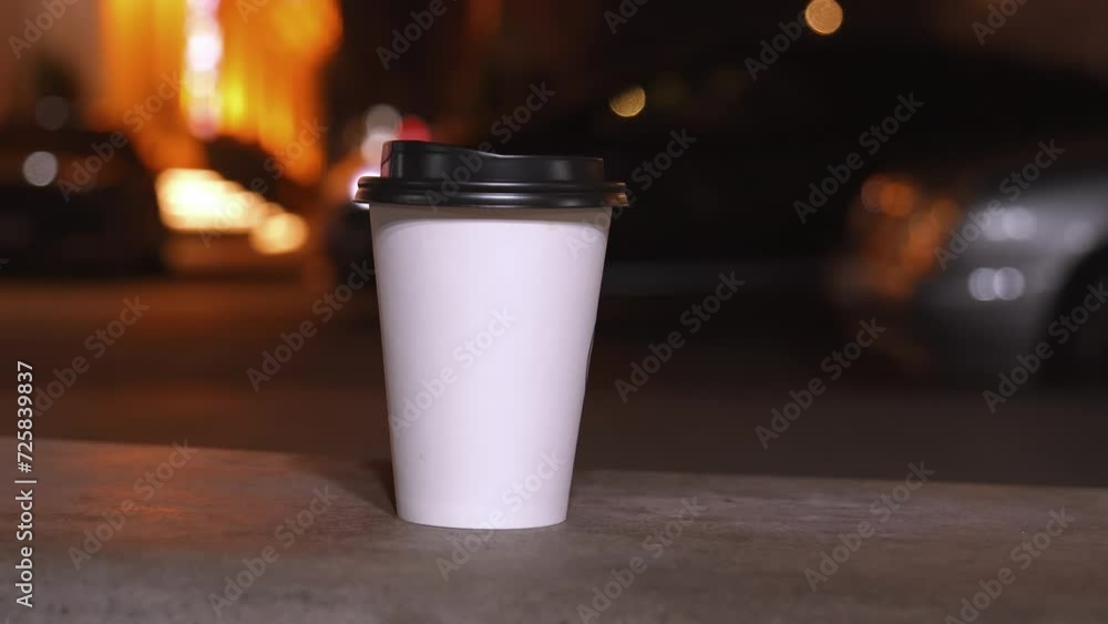 Two white paper disposable cups on blurred background of evening city lights. Female unrecognizable hand taking one cup of coffee. Hot Takeaway Coffee Outdoors. Street food,