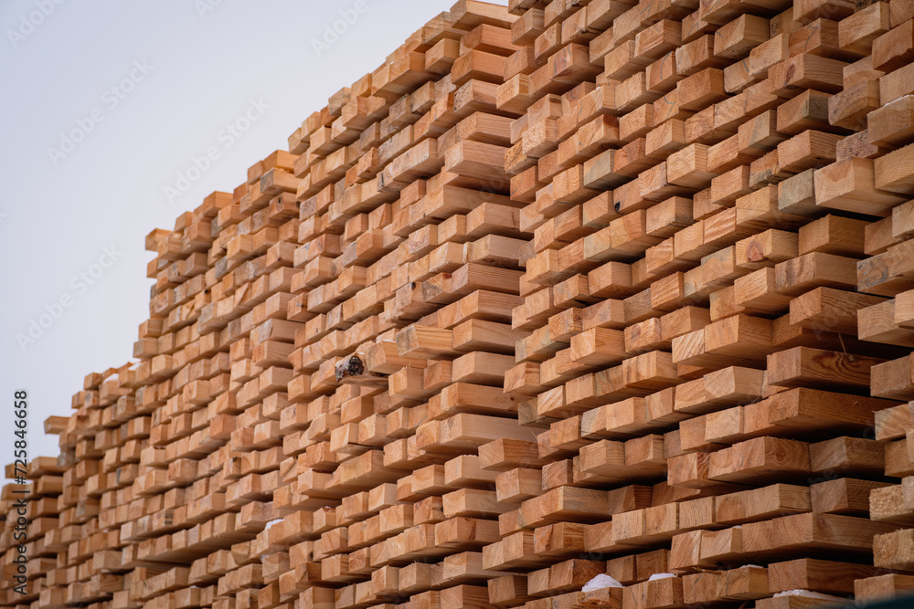A pile of wood with a layer of snow on top, showcasing the wintry weather conditions. A tall and sturdy pile of wooden planks stacked atop one another in a stable manner.