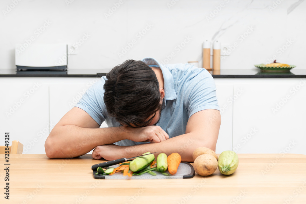 Fototapeta premium Tired and sad man peeling vegetables in the kitchen