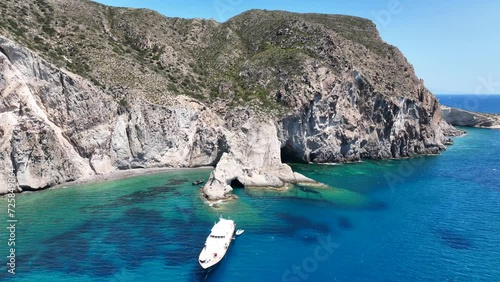 Aerial drone video of beautiful turquoise beach and cave formations visited by yachts and sailboats in Southern part of Antiparos island, Cyclades, Greece photo