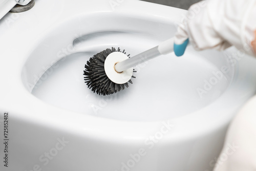 Сlose-up shot of a housewife in rubber gloves cleaning a toilet using a special cleaning product and a brush photo