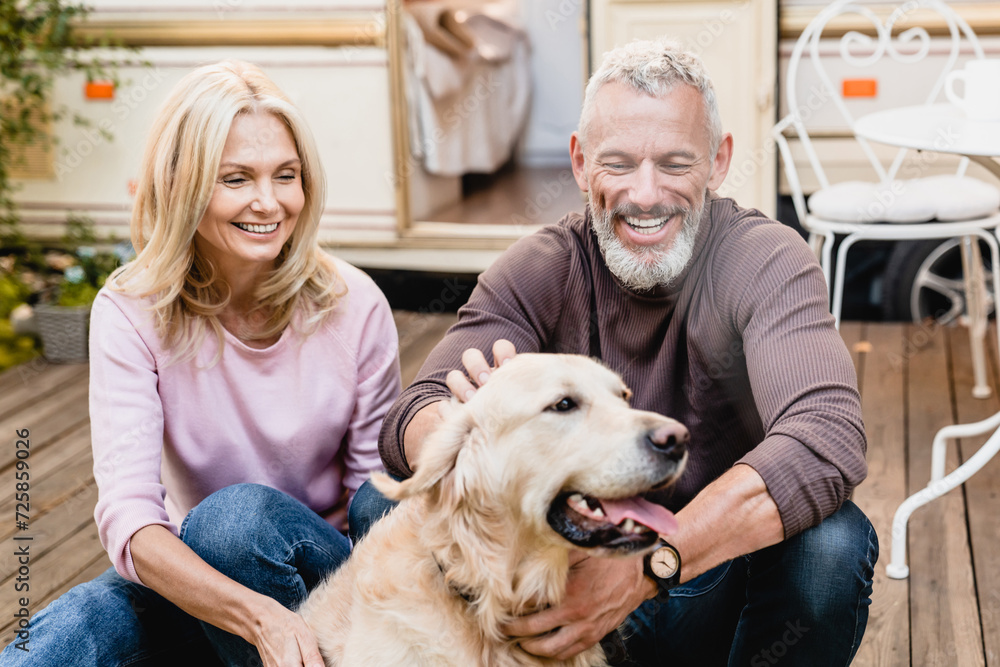 Glad mature caucasian couple spouses husband and wife spending their free time with dog in the van yard, traveling together with a pet golden retriever labrador