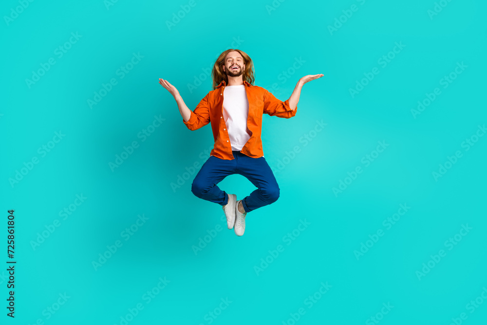 Full length photo of positive man dressed orange shirt flying arms comparing products empty space isolated on teal color background
