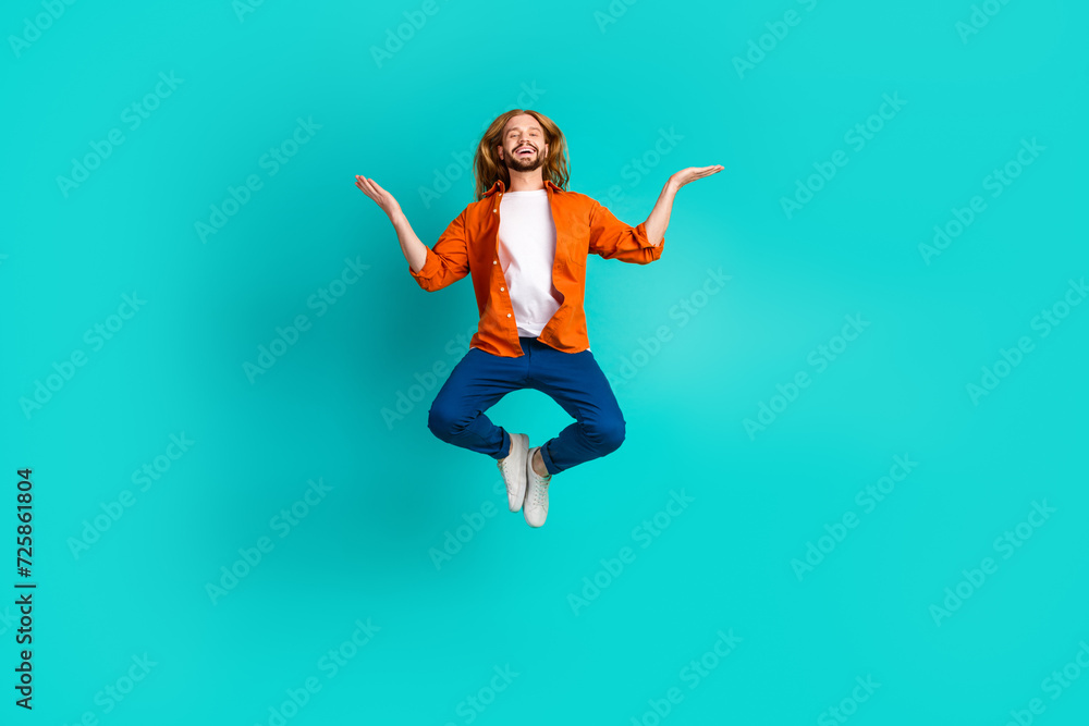 Full length photo of positive man dressed orange shirt flying arms comparing products empty space isolated on teal color background Full length photo of positive man dressed orange shirt flying arms comparing products empty space isolated on teal color background