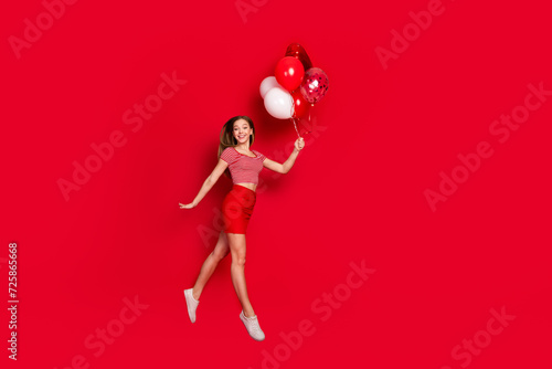 Full length photo of sweet pretty lady dressed striped top enjoying birthday party flying balloons empty space isolated red color background