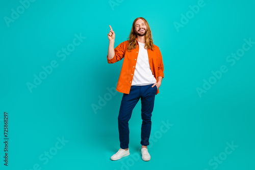 Full body length photo of young blond man in orange shirt blue pants point finger presentation mockup isolated on cyan color background