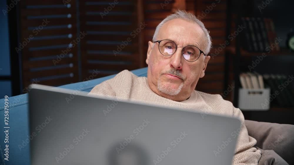 Elderly man working remotely from home, portrait of person with laptop in evening in living room Elderly man working remotely from home, portrait of person with laptop in evening in living room