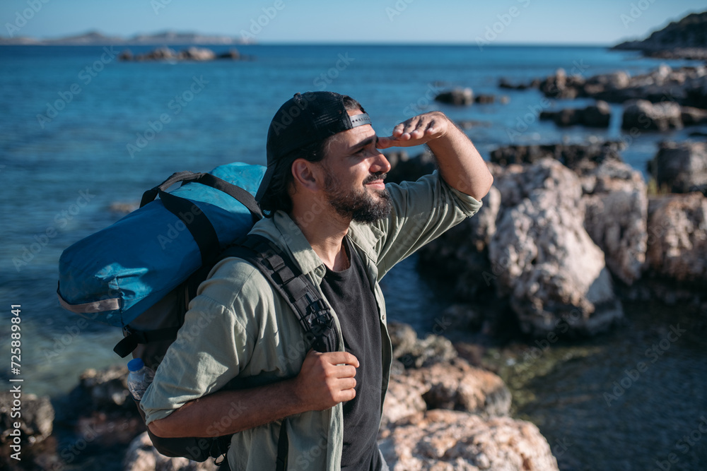 Obraz premium A male tourist with a large backpack and hiking gear on a rocky seashore.