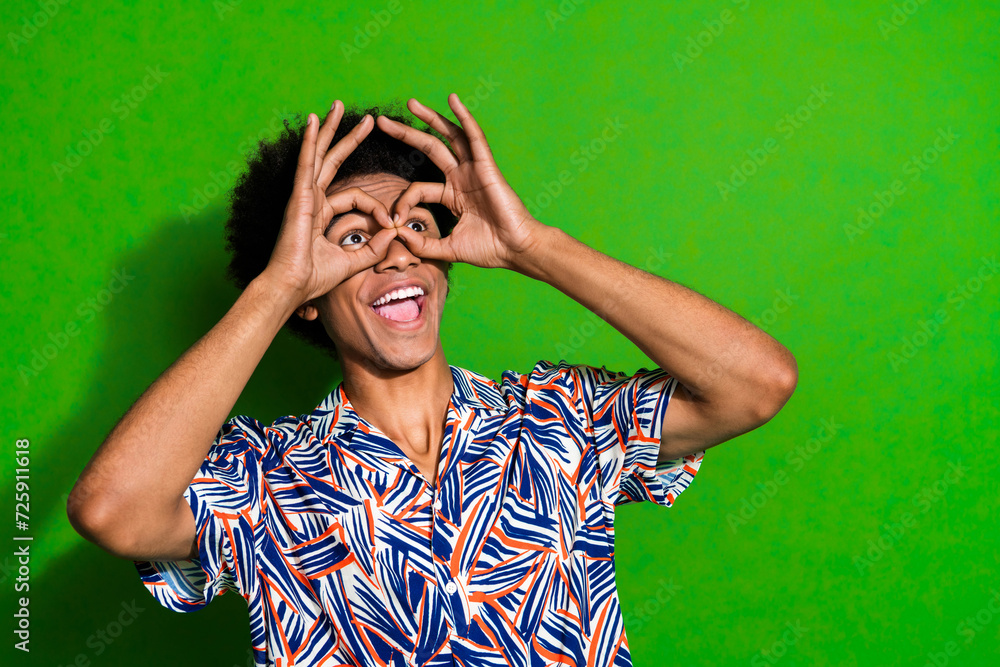 Photo of funky young guy made creative goggles his fingers looking empty space searching adventures isolated on green color background Photo of funky young guy made creative goggles his fingers looking empty space searching adventures isolated on green color background