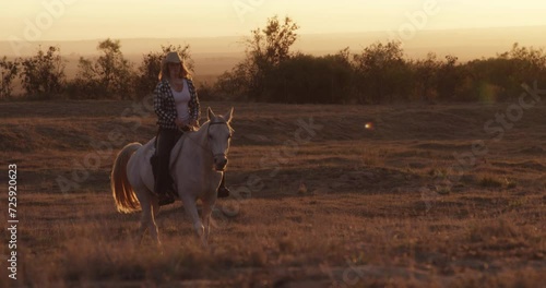 Sunset, horse riding or woman in ranch or nature with rider or jockey for adventure or wellness. Travel, freedom or cowgirl with a healthy pet animal for training, exercise or peace on farm or field photo