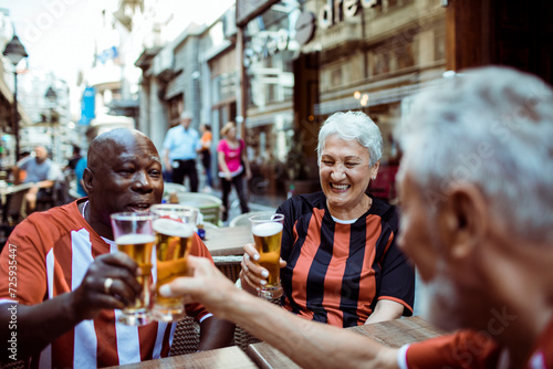 Group of seniors in sports jerseys having beer in an outdoor cafe or bar