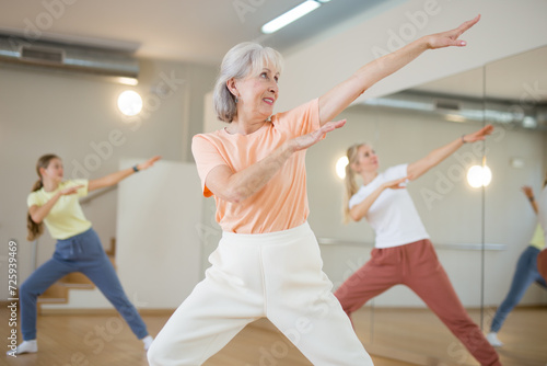 Portrait of cheerful active female pensioner exercising dance moves in fitness studio