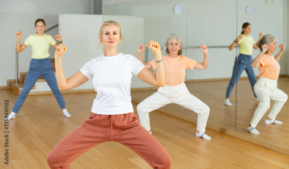 Fototapeta premium Woman doing squats with her family on group fitness training in studio.