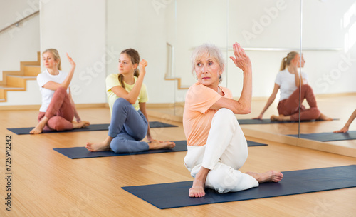 Young sporty girl with her mother and grandmother performing yoga in fitness studio