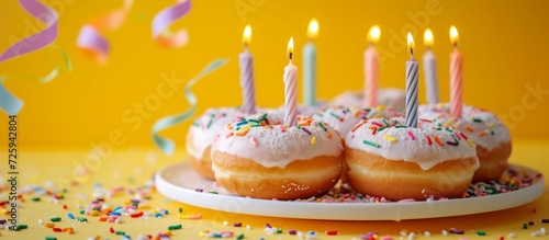 Powder fly in celebration of birthday on yellow backdrop with candles atop donuts.