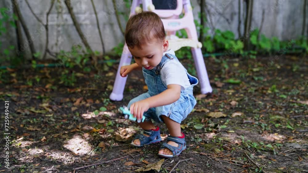 Charming Caucasian boy in jeans romper plays with a toy car outdoors. Kid's blackboard at backdrop. Charming Caucasian boy in jeans romper plays with a toy car outdoors. Kid's blackboard at backdrop.