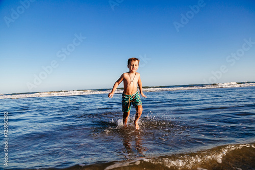 Kid bathing in the sea. Boy having fun in the ocean waves at sunset on a sunny summer vacation day. Child having fun outdoors.