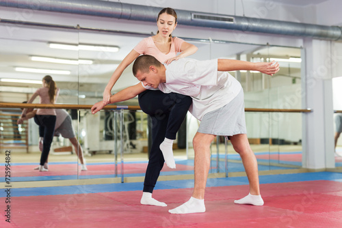 Caucasian woman performing knee strike while sparring with man in gym during self-defence training.
