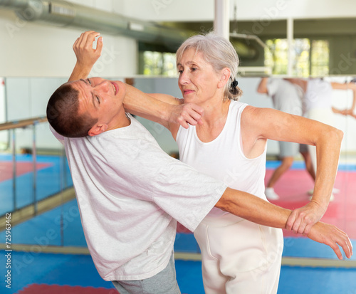 Elderly woman is training with man on the self-defense course in gym