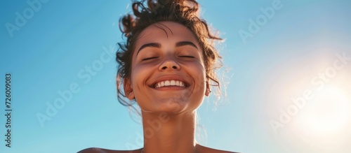Fit young woman smiles while deep breathing in front of a clear blue sky on a sunny and windy summer day. photo