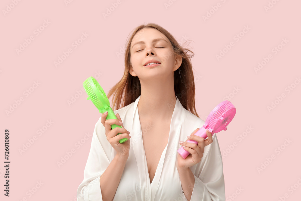 Beautiful young woman with handheld mini fans on pink background Beautiful young woman with handheld mini fans on pink background