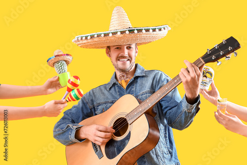 Fotografija Young man playing guitar and hands with Mexican symbols on yellow background