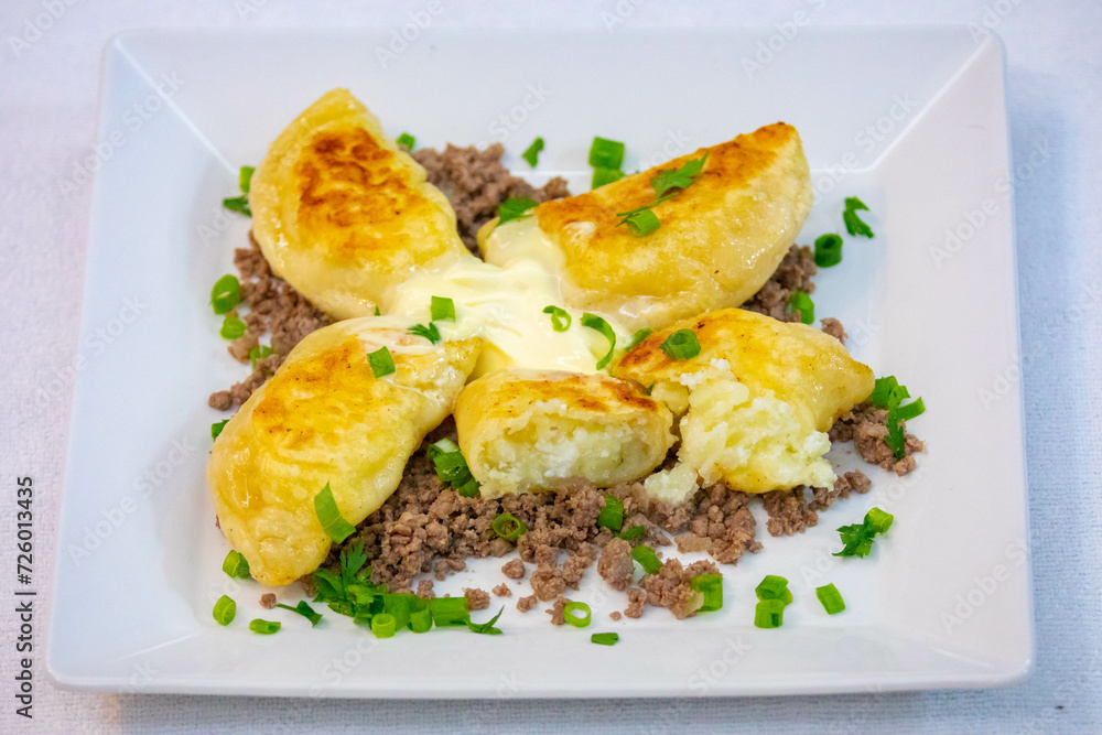 Traditional Ukrainian pierogi grilled in butter and served with minced meat and cream, decorated with fresh fine herbs Traditional Ukrainian pierogi grilled in butter and served with minced meat and cream, decorated with fresh fine herbs
