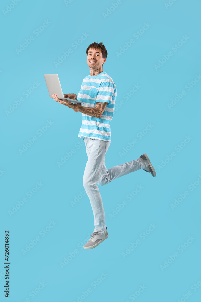 Happy young man with modern laptop jumping on blue background Happy young man with modern laptop jumping on blue background