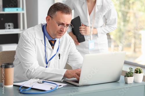 Mature doctor and his assistant working with laptop in medical office