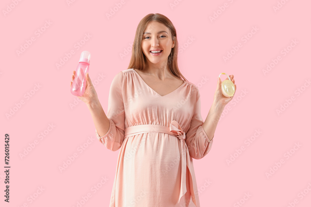 Young pregnant woman with baby bottle and pacifier on pink background Young pregnant woman with baby bottle and pacifier on pink background
