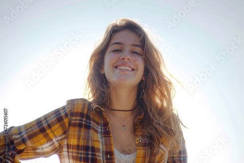 A woman wearing a plaid shirt and a necklace smiles for the camera