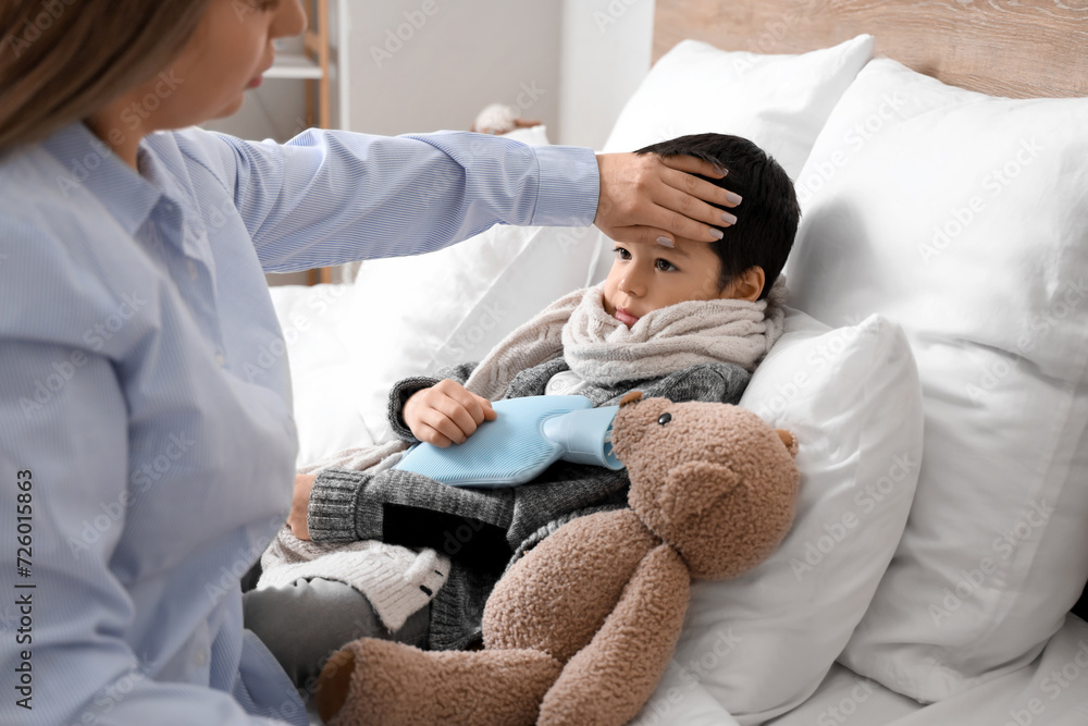 Mother touching forehead of her ill little son in bedroom Mother touching forehead of her ill little son in bedroom