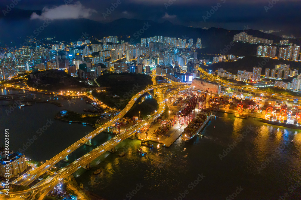 Fototapeta premium Aerial top view of container cargo ship in the export and import business and logistics international goods in urban city. Shipping to the harbor by crane in Victoria Harbour, Hong Kong City at night.