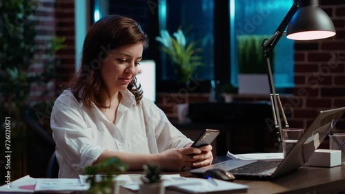 Smiling manager looking at text messages on smartphone, taking break from working on company project. Team leader unwinding by using phone to browse social media in office, camera B