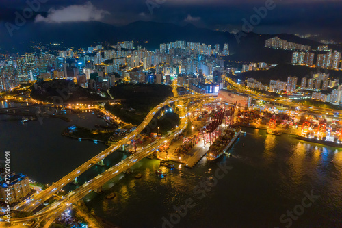 Aerial top view of container cargo ship in the export and import business and logistics international goods in urban city. Shipping to the harbor by crane in Victoria Harbour, Hong Kong City at night.